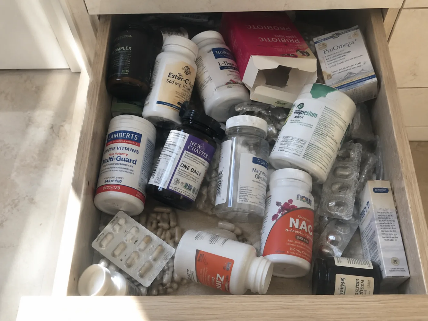 A drawer crammed with mismatched, unlabelled supplement bottles, blister packs and loose capsules